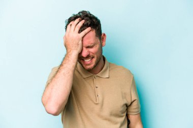 Kafkasyalı genç adam mavi arka planda izole edilmiş bir şekilde bir şeyi unutuyor. Alnına avuç içi ve gözlerini kapayarak vuruyor..
