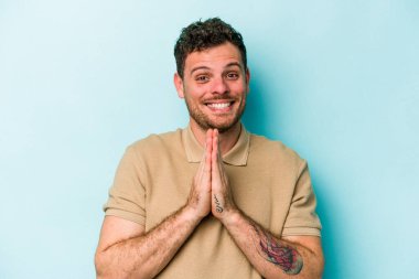 Mavi arka planda izole edilmiş genç beyaz bir adam el ele tutuşup, ağzının kenarında dua ediyor, kendinden emin..
