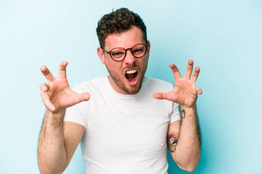 Mavi arka planda izole edilmiş genç beyaz adam gergin elleriyle çığlık atıyor..