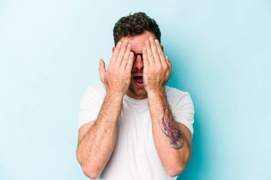 Mavi arka planda izole edilmiş genç beyaz adam yüzünün yarısını palmiye ile kaplayarak eğleniyor..