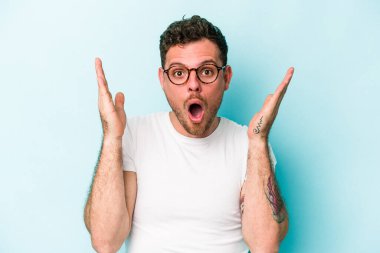 Kafkasyalı genç adam mavi arka planda izole edildi. Şaşırdı ve şok oldu..