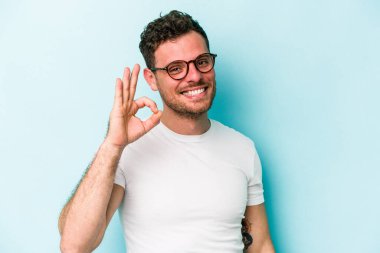 Kafkasyalı genç adam mavi arka planda izole edilmiş neşeli ve kendinden emin..