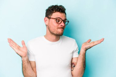 Kafkasyalı genç adam mavi arka planda izole edilmiş. Kafası karışmış ve omuz silkiyor. Kopya alanını tutmak için..