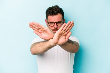 Kafkasyalı genç adam mavi arka planda izole edilmiş bir şekilde inkar hareketi yapıyor.