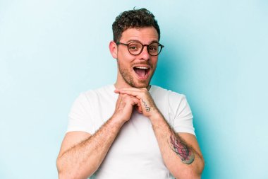 Kafkasyalı genç adam mavi arka planda izole edilmiş şans için dua ediyor, şaşırmış ve ağzını açıp önüne bakıyor..