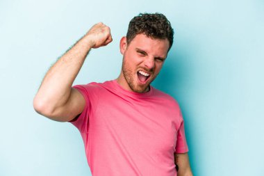 Mavi arka planda izole edilmiş genç beyaz bir adam zaferi, tutkuyu ve coşkuyu kutluyor, mutlu bir ifade..