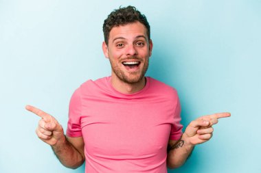 Mavi arka planda izole edilmiş genç beyaz adam farklı kopya alanlarını gösteriyor, birini seçiyor, parmaklarıyla gösteriyor.