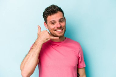 Mavi arka planda izole edilmiş genç beyaz adam parmaklarıyla bir cep telefonu hareketi gösteriyor..
