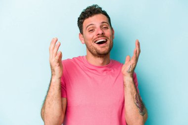 Mavi arka planda izole olmuş genç beyaz adam yüksek sesle gülüyor ve elini göğsüne koyuyor..