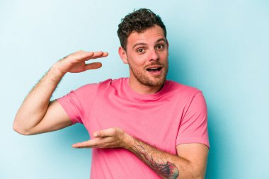Mavi arka planda izole genç beyaz adam iki eliyle bir şey tutuyor, ürün sunumu..