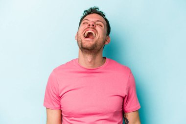 Kafkasyalı genç adam mavi arka planda izole edilmiş rahat ve mutlu bir şekilde gülüyor, boynunda dişlerini gösteriyor..