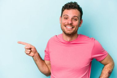 Mavi arka planda izole edilmiş genç beyaz adam işaret parmağıyla işaret ederek gülümsüyor..