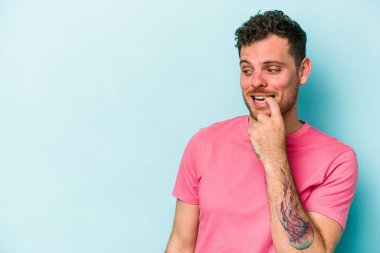 Mavi arka planda izole edilmiş genç beyaz adam rahatlamış bir şeyin fotokopi odasına baktığını düşünüyor..