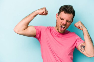 Mavi arka planda izole edilmiş genç beyaz bir adam zaferden sonra yumruğunu kaldırıyor, kazanan konsept..