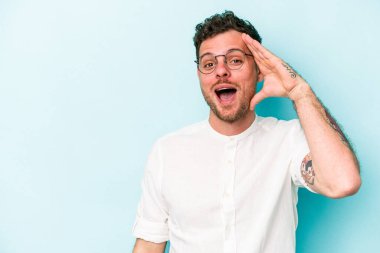 Mavi arka planda izole edilmiş genç beyaz adam yüksek sesle bağırıyor, gözleri açık ve elleri gergin tutuyor..