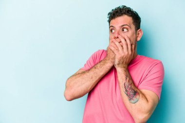 Kafkasyalı genç adam mavi arka planda izole edilmiş. Düşünceli bir şekilde ağzıyla ağzını kapatan bir fotokopi odasına bakıyor..