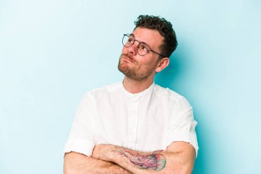 Kafkasyalı genç adam mavi arka planda izole edilmiş hedeflerine ve amaçlarına ulaşma hayali kuruyor.