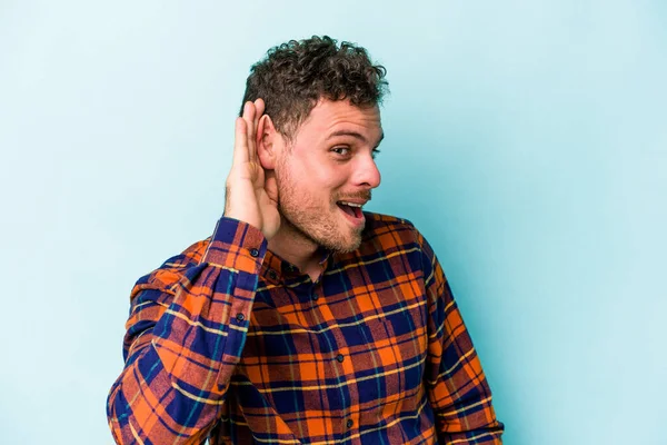 Mavi arka planda izole edilmiş genç beyaz adam bir dedikoduyu dinlemeye çalışıyor..