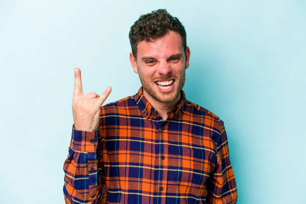 Mavi arka planda izole edilmiş genç beyaz adam boynuzlarını devrim konsepti olarak gösteriyor..