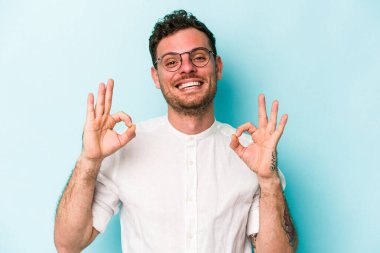 Kafkasyalı genç adam mavi arka planda izole edilmiş neşeli ve kendinden emin..