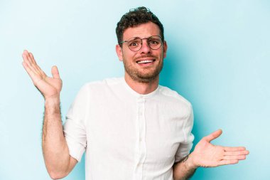 Kafkasyalı genç adam mavi arka planda izole edilmiş. Kafası karışmış ve omuz silkiyor. Kopya alanını tutmak için..