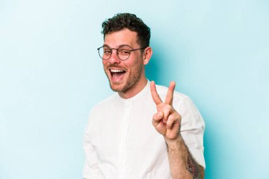 Mavi arka planda izole edilmiş genç beyaz adam iki numarayı parmaklarıyla gösteriyor..