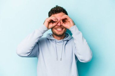 Mavi arka planda izole edilmiş genç beyaz adam gözlerinde sorun olmadığını gösteriyor.