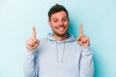 Mavi arka planda izole genç beyaz adam işaret iki ön parmakları boş bir boşluk gösteren.