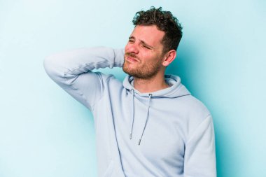 Kafkasyalı genç adam mavi arka planda izole edilmiş dirsek masajı yapıyor, kötü bir hareketin ardından acı çekiyor..