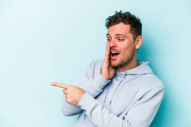 Kafkasyalı genç adam mavi arka planda izole edilmiş. Dedikodu yapıyor, bir şeyleri bildiriyor..