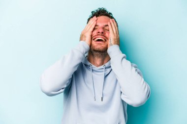 Mavi arka planda izole edilmiş genç beyaz adam ellerini başının üstünde tutarak neşe içinde gülüyor. Mutluluk kavramı.