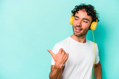 Mavi arka planda müzik dinleyen beyaz bir adam. Baş parmak uzakta, gülüyor ve kaygısız..