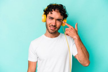 Mavi arka planda izole edilmiş müzik dinleyen beyaz bir adam işaret parmağıyla yaptığı hayal kırıklığı jestini gösteriyor..