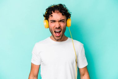 Mavi arka planda izole edilmiş müzik dinleyen genç beyaz adam çok sinirli ve agresif çığlıklar atıyor..