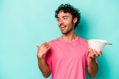 Mavi arka plan noktalarında izole edilmiş erişte yiyen genç beyaz adam başparmak uzakta, gülüyor ve kaygısız..