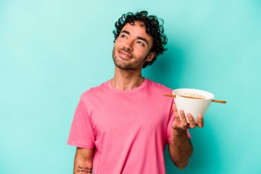 Mavi arka planda izole edilmiş erişte yiyen genç beyaz adam amaçlarına ve amaçlarına ulaşmayı hayal ediyor.