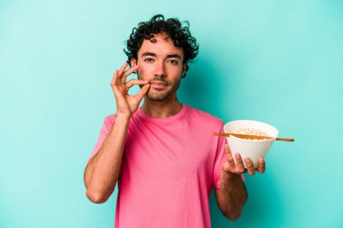 Mavi arka planda izole edilmiş erişte yiyen genç beyaz adam dudaklarında parmaklarıyla bir sır saklıyor..