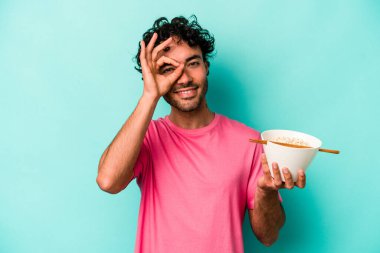 Mavi arka planda izole edilmiş erişte yiyen genç, beyaz bir adam heyecanlı..