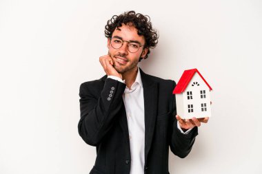 Beyaz arka planda izole edilmiş, tırnak yiyen, gergin ve endişeli bir oyuncak evi tutan Kafkasyalı genç bir iş adamı..