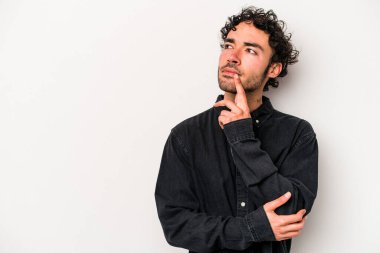 Beyaz arka planda izole edilmiş genç beyaz bir adam şüpheli ve şüpheci bir ifadeyle yana bakıyor..