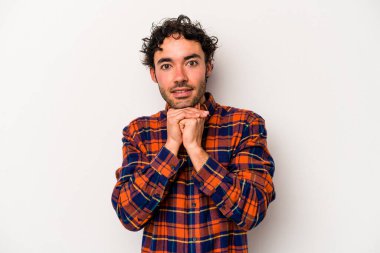 Beyaz arka planda izole edilmiş genç beyaz bir adam şans için dua ediyor, şaşırmış ve ağzını açıp önüne bakıyor..