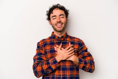 Beyaz arka planda soyutlanmış beyaz tenli genç bir adam gülüyor, elini yüreğine koyuyor, mutluluk kavramını koruyor..