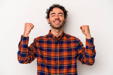 Beyaz arka planda izole edilmiş genç beyaz bir adam zaferi, tutkuyu ve coşkuyu kutluyor, mutlu bir ifade..