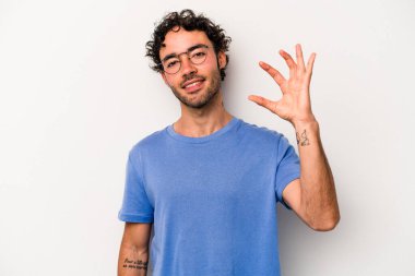 Beyaz arka planda izole edilmiş genç beyaz bir adam işaret parmaklarıyla küçük bir şey tutuyor, gülümsüyor ve kendinden emin..