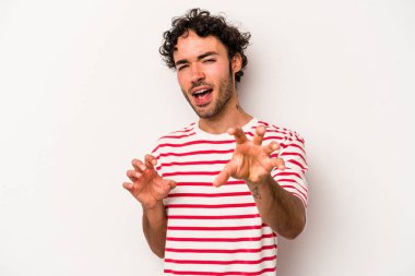 Beyaz arka planda izole edilmiş genç beyaz bir adam pençelerini kedi taklidi yaparken gösteriyor, agresif bir hareket..