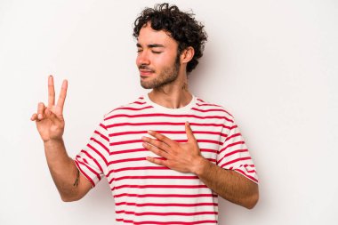 Beyaz arka planda izole edilmiş genç beyaz adam yemin ediyor, elini göğsüne koyuyor..