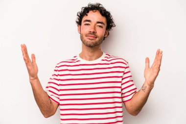 Beyaz arka planda izole edilmiş genç beyaz bir adam işaret parmaklarıyla küçük bir şey tutuyor, gülümsüyor ve kendinden emin..