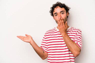 Beyaz arka planda izole edilmiş genç beyaz adam, avuç içi fotokopi alanını elinde tutmaktan etkilenmiş..