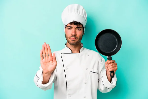 年轻的高加索厨师拿着用蓝色背景隔开的飞行锅 伸出的手显示出停止的迹象 阻止了你 — 图库照片