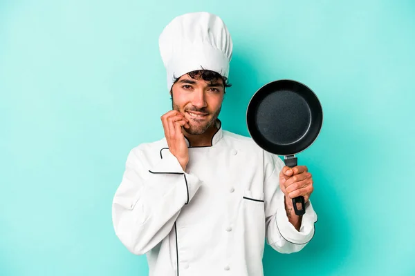 年轻的高加索厨师拿着用蓝色底咬指甲隔离的飞盘 紧张而焦虑 — 图库照片